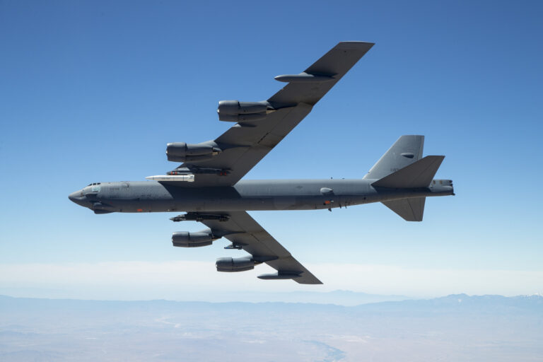 B-52 Stratofortress bomber in flight over the desert, carrying a test missile under its wing